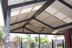 A modern verandah with a sleek Colorbond roof and sturdy posts, extending over a stylish outdoor space. The verandah features a combination of Fibreglass and Colorbond materials, providing shade and enhancing the home’s exterior design.