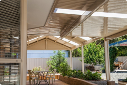 A modern Colorbond verandah with a sleek design, featuring a combination of Bluescope steel and Fibreglass roofing. The verandah extends over a spacious outdoor patio, enhancing the home's outdoor space.