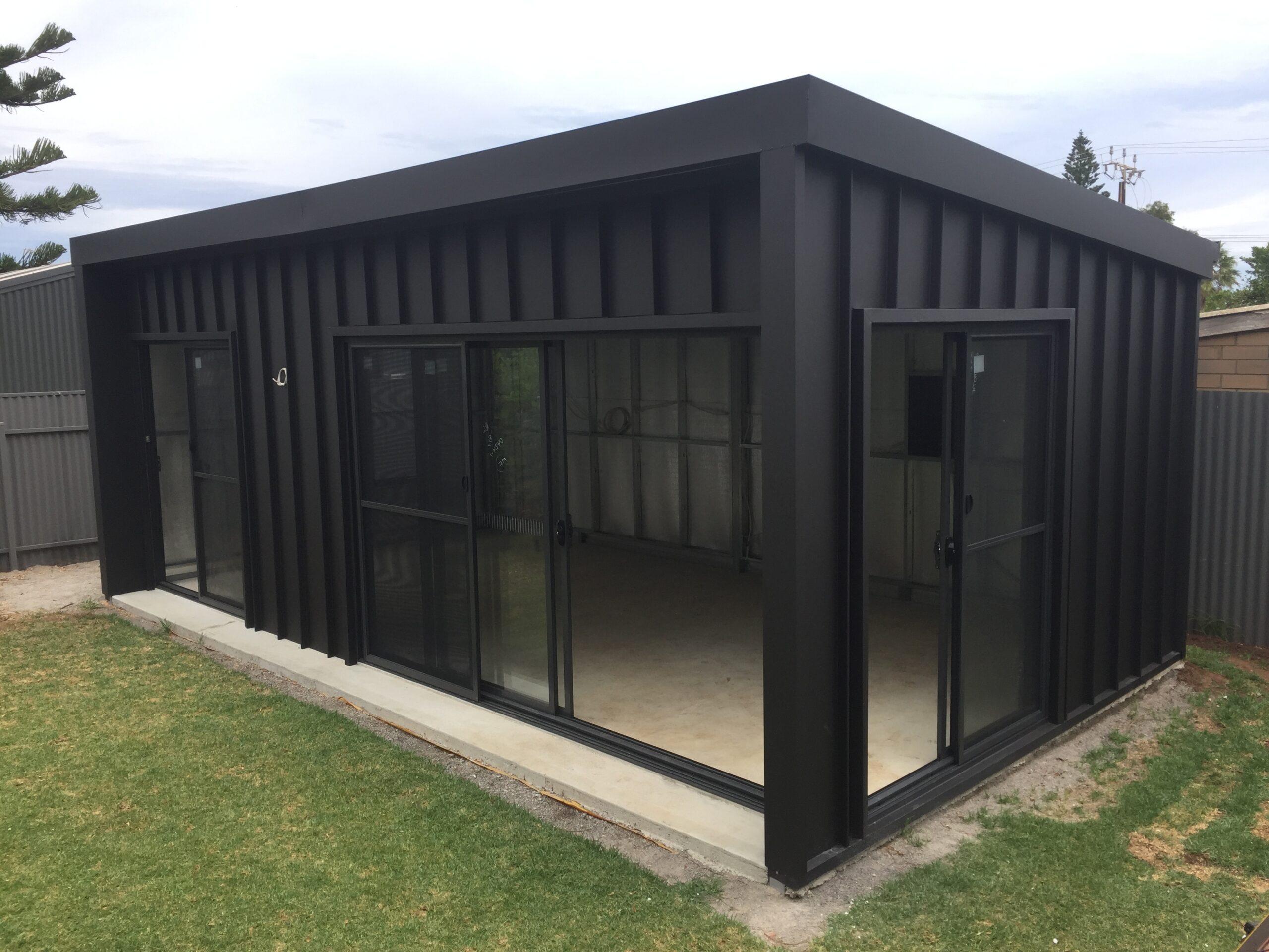 A large custom steel shed with a sleek shed roof, blending timber and steel materials, situated in a well-maintained garden area.
